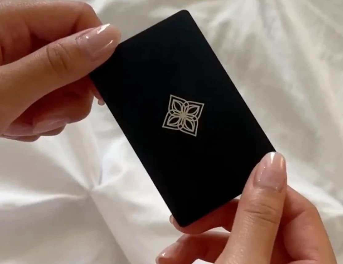 Hands holding a black Bloom Card over white bedding