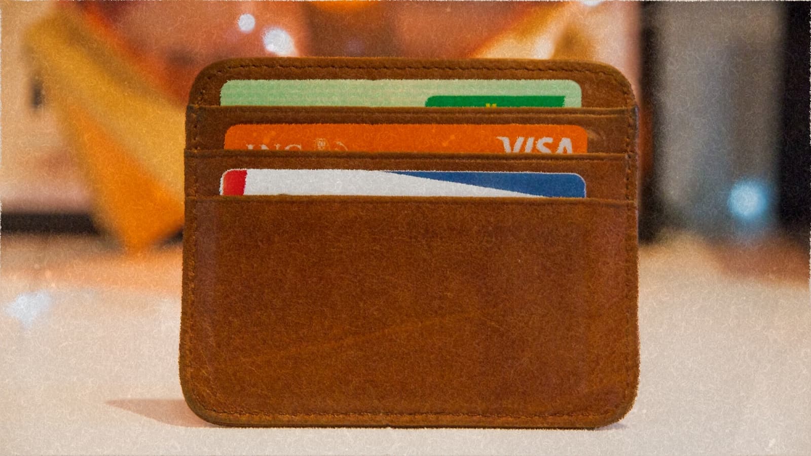 A leather card wallet holding a Visa card and two others, on a warm-lit counter.