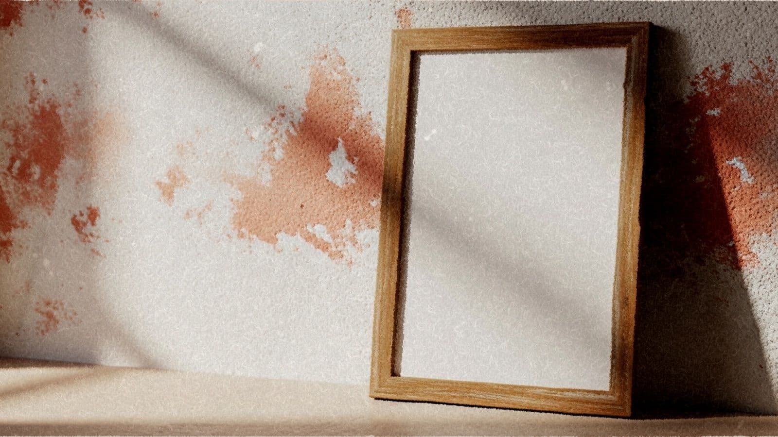 An empty vintage wooden poster frame leaning on a warm plaster wall.
