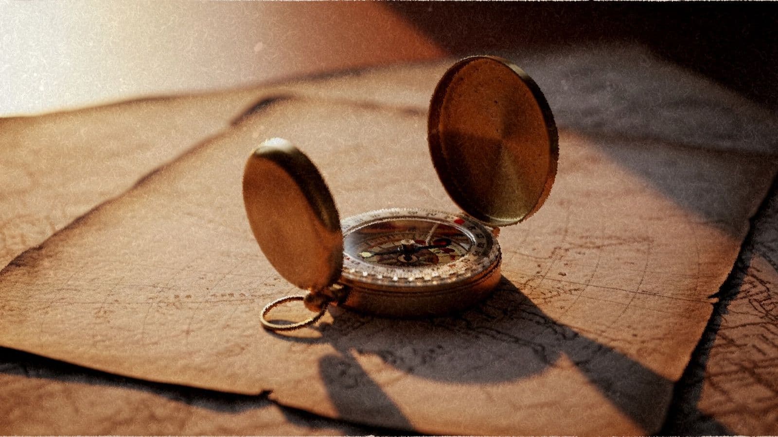A brass compass resting on a weathered paper map in warm window light.