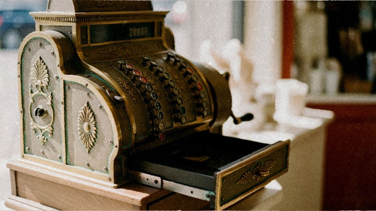 An antique brass cash register with its drawer slightly open.