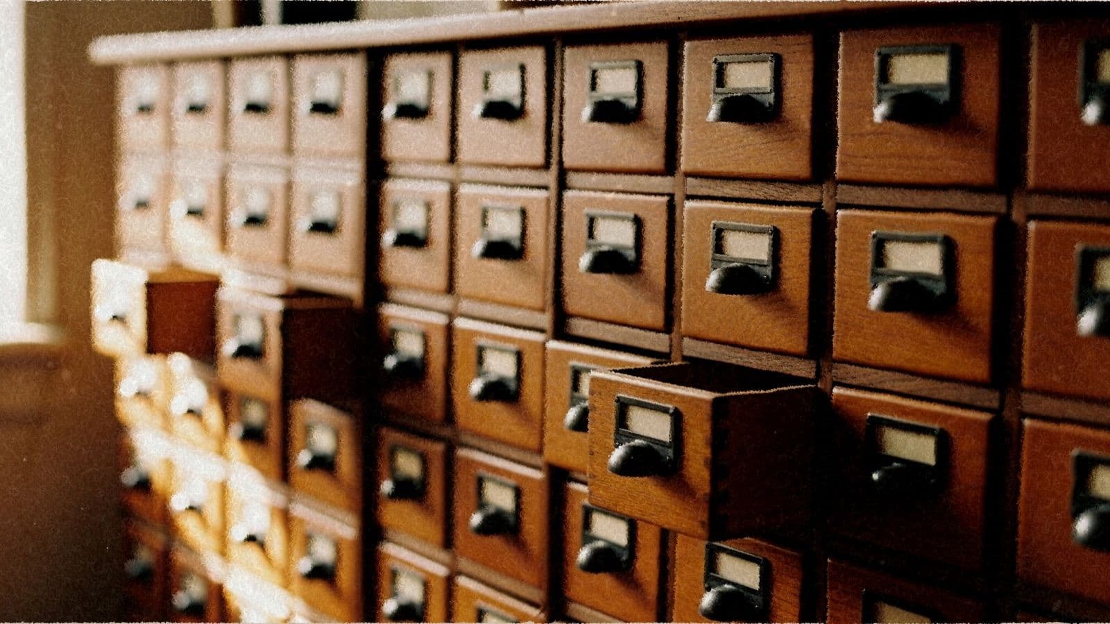 An apothecary cabinet of small wooden drawers, a few open, in warm light.